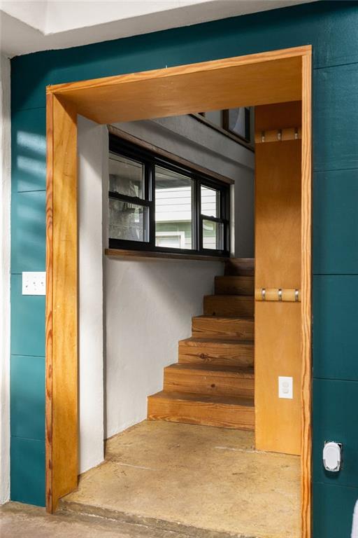 Wooden staircase beside black-framed windows, viewed through a natural wood-trimmed doorway.