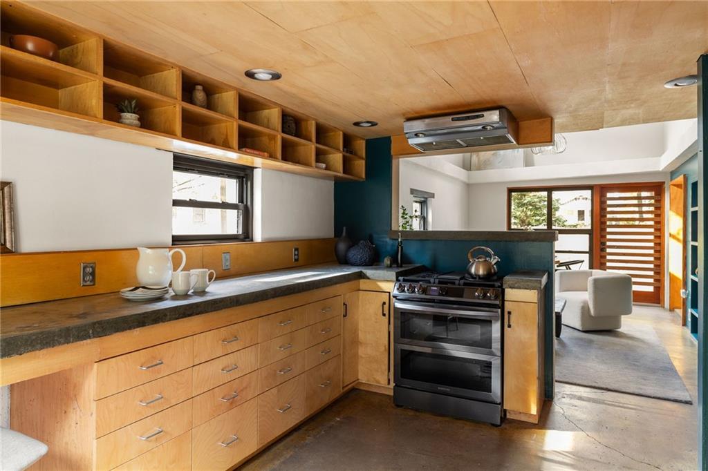 Kitchen with warm wood cabinets, open shelving, concrete counters, and a stainless steel range.