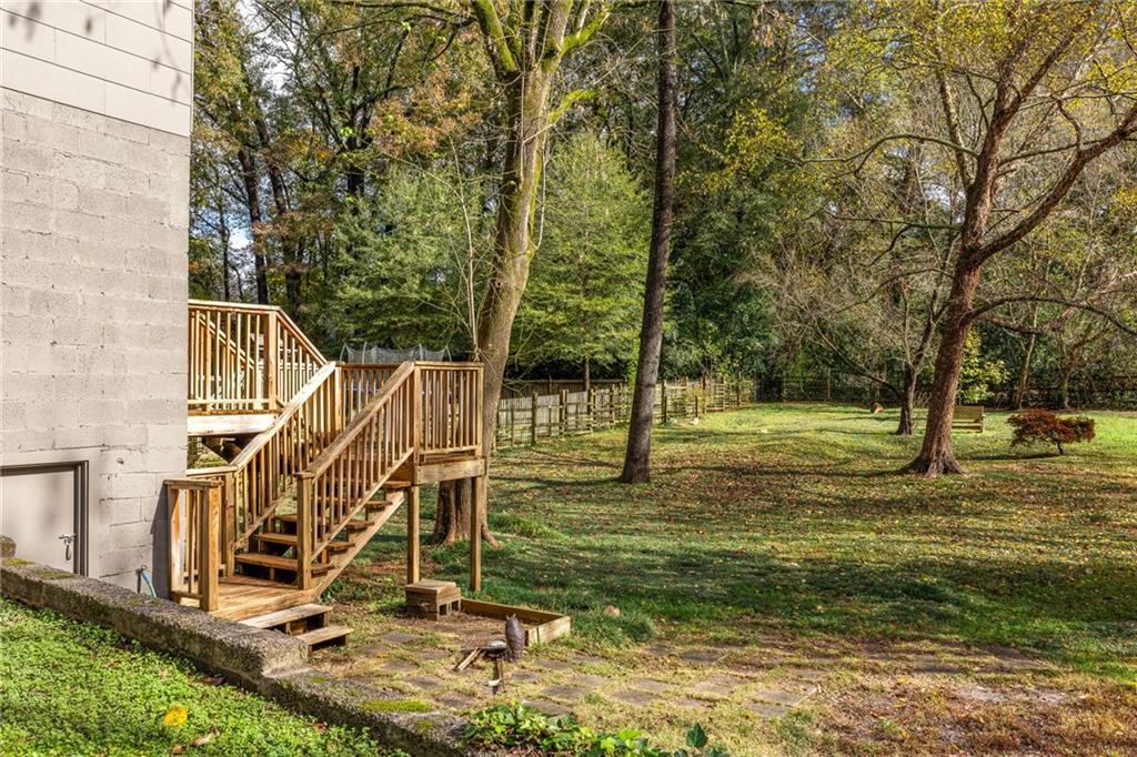Backyard with a raised wooden deck, stairs, and mature trees along a fenced lawn.