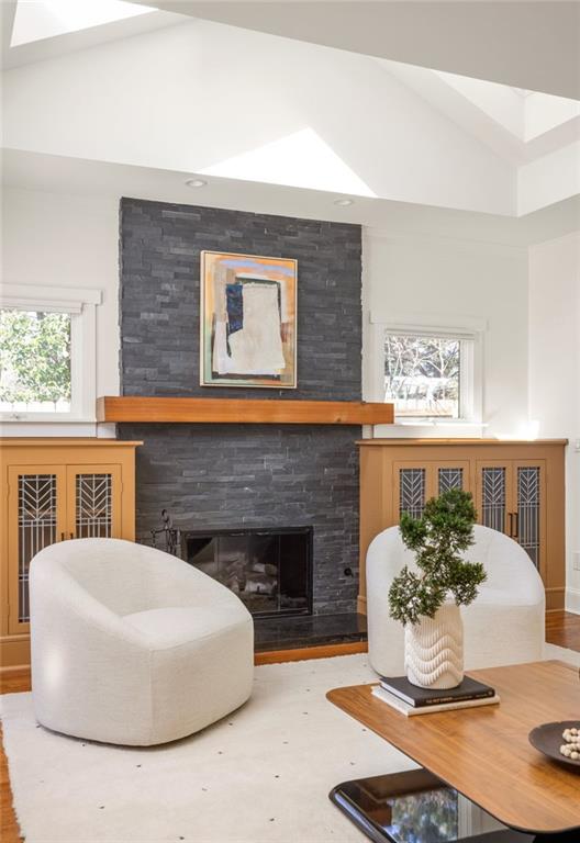 Living room with a vaulted ceiling, dark stone fireplace, and two white curved chairs.