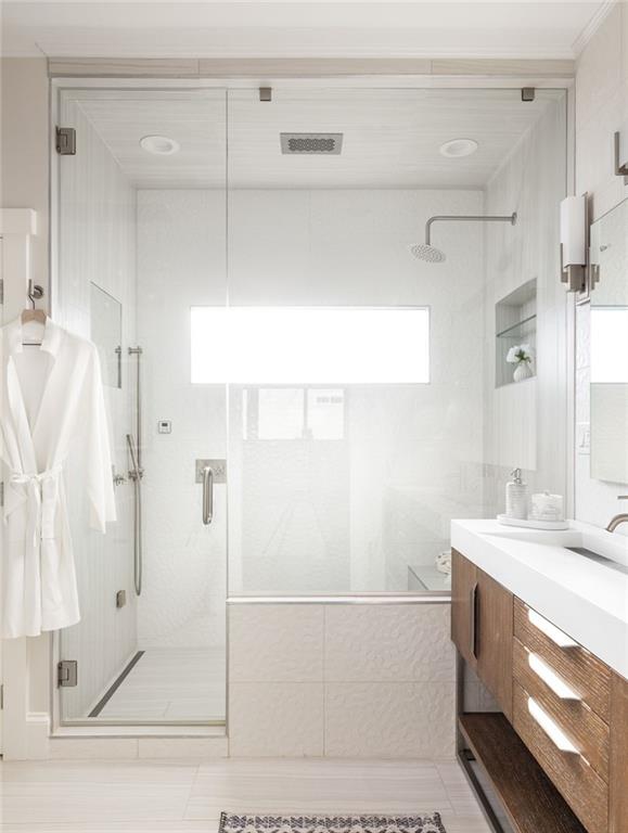 Bright bathroom with a glass walk-in shower, long window, and wood vanity.