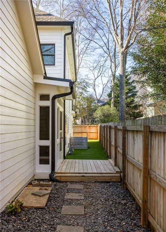 House side yard with a small deck, artificial turf, and a gravel path between wooden fences.