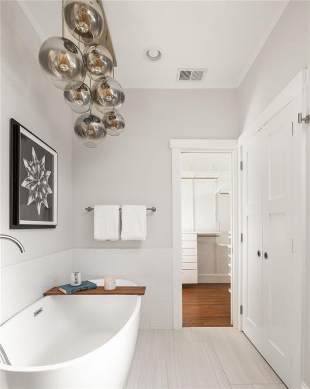 Modern bathroom with a freestanding soaking tub and glass globe chandelier beside an open walk-in closet.