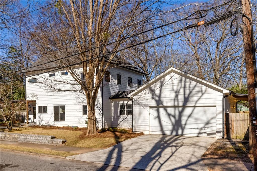 White two-story house with an attached garage, driveway, leafless trees, and overhead utility wires.