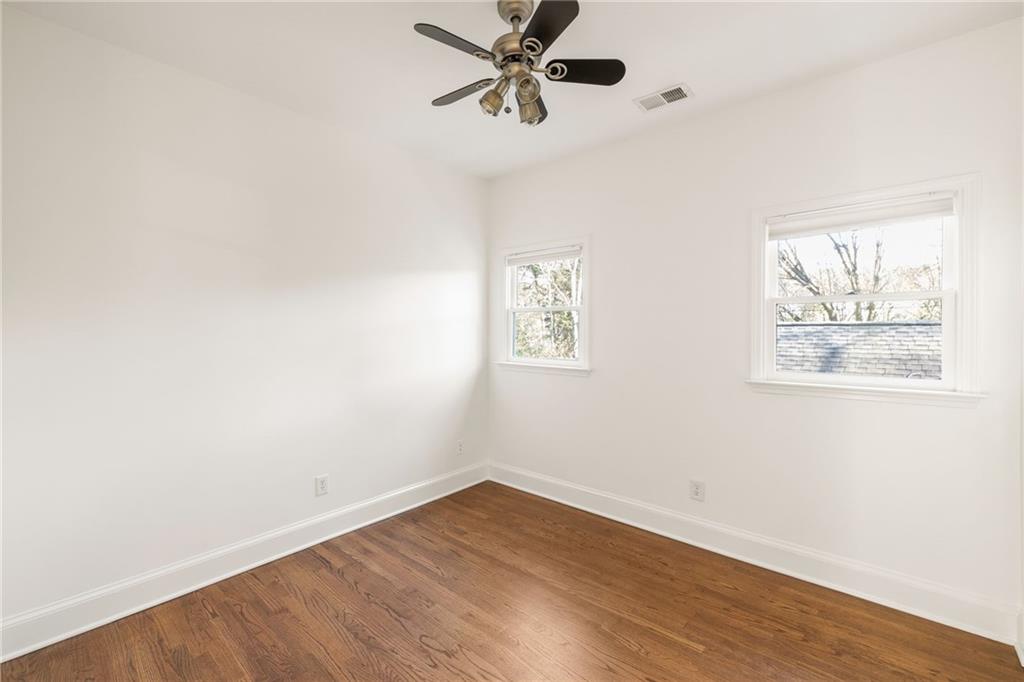 Empty bedroom with hardwood floors, a ceiling fan, and two windows.