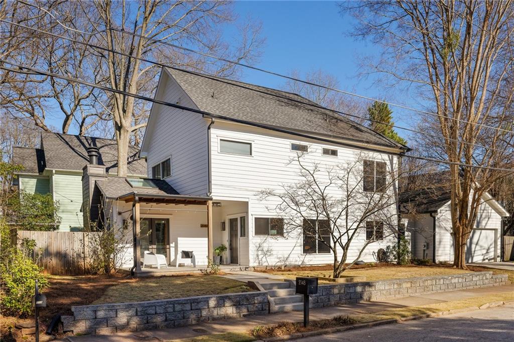 White two-story house with a covered patio, stone retaining wall, and leafless trees.