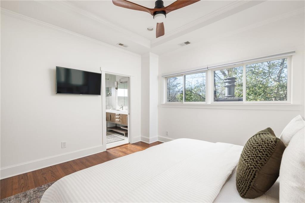 Bright bedroom with a wide tree-view window, hardwood floors, and an open doorway to the bathroom.