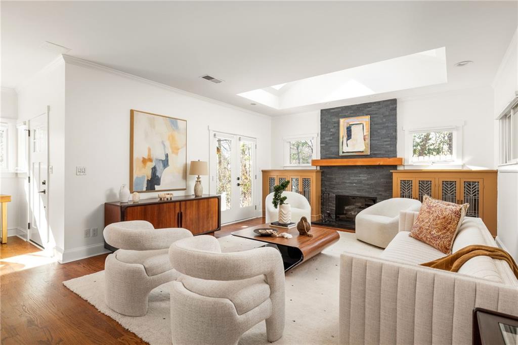 Bright living room with white seating, hardwood floors, and a dark brick fireplace beneath a skylight.