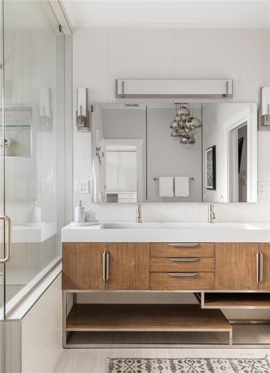 Modern bathroom with a wide wood vanity, double sinks, large mirror, and glass-enclosed shower.