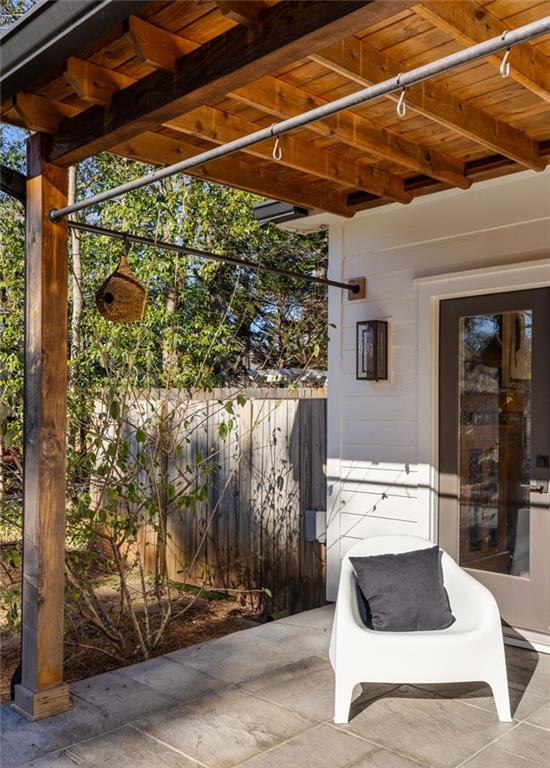 Covered patio with a wood-beam ceiling, white lounge chair, and fenced garden.