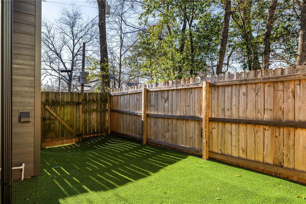 Fenced backyard with green artificial turf and tall wooden privacy fencing.