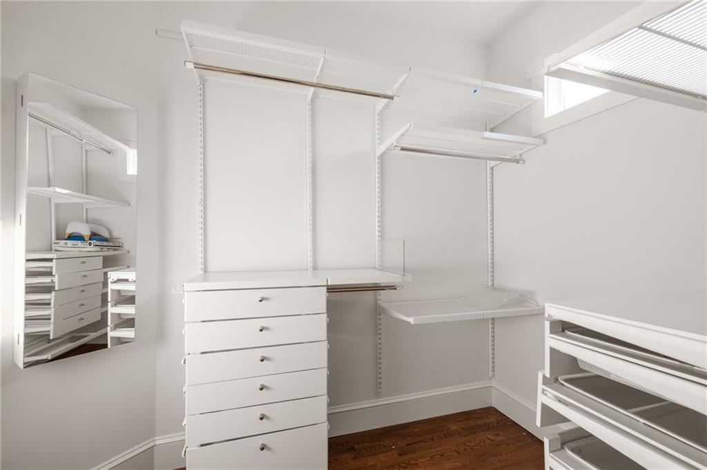 Walk-in closet with white built-in shelving, pull-out baskets, and a central drawer unit.