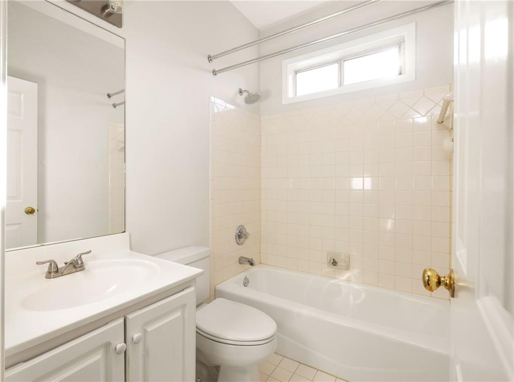 Bathroom with a white vanity, toilet, and bathtub beneath a high window.