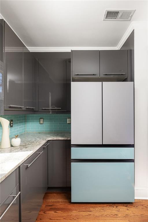 Kitchen with dark cabinetry, turquoise tile backsplash, white counters, and hardwood flooring.