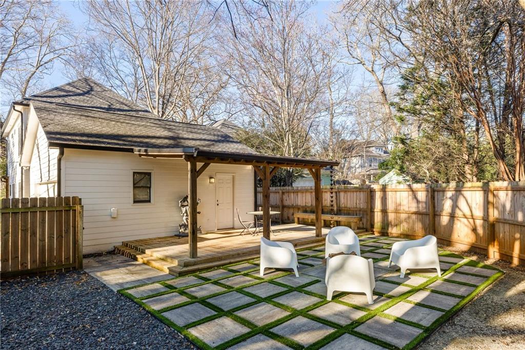 House backyard with a covered patio and white chairs on a grass-lined paved seating area.
