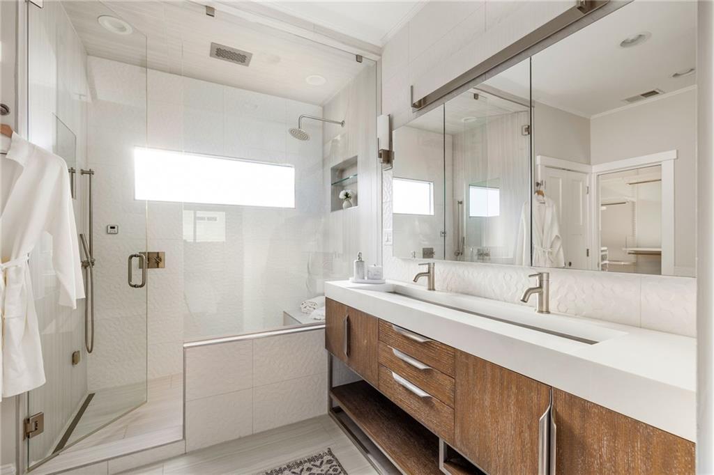 Bright bathroom with a glass-enclosed shower and long double-sink wood vanity.