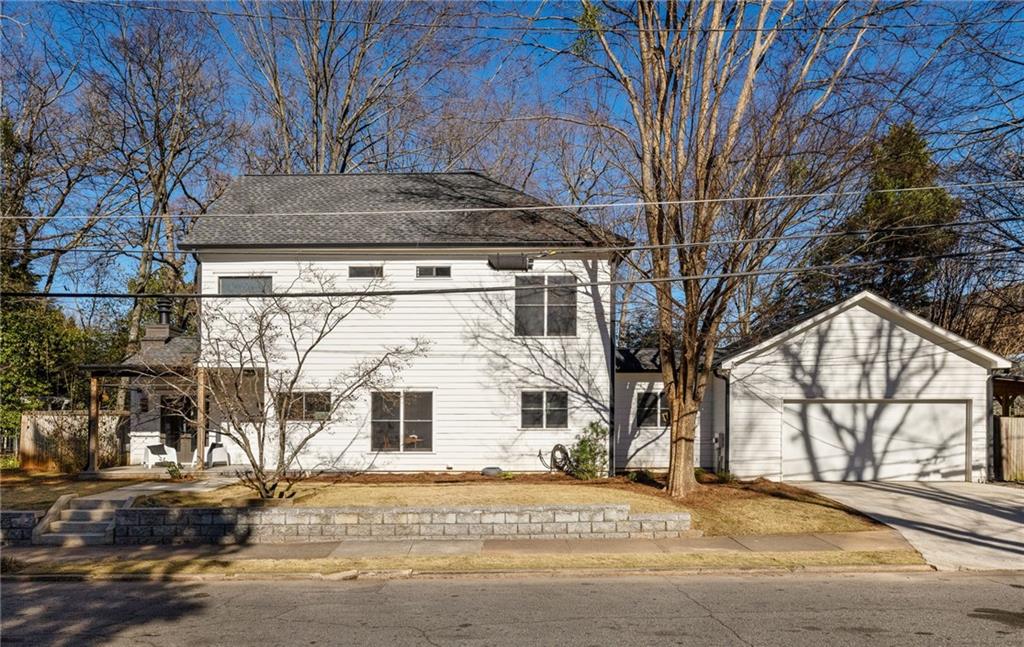 White two-story house with an attached garage and stone retaining wall, viewed from the rear.