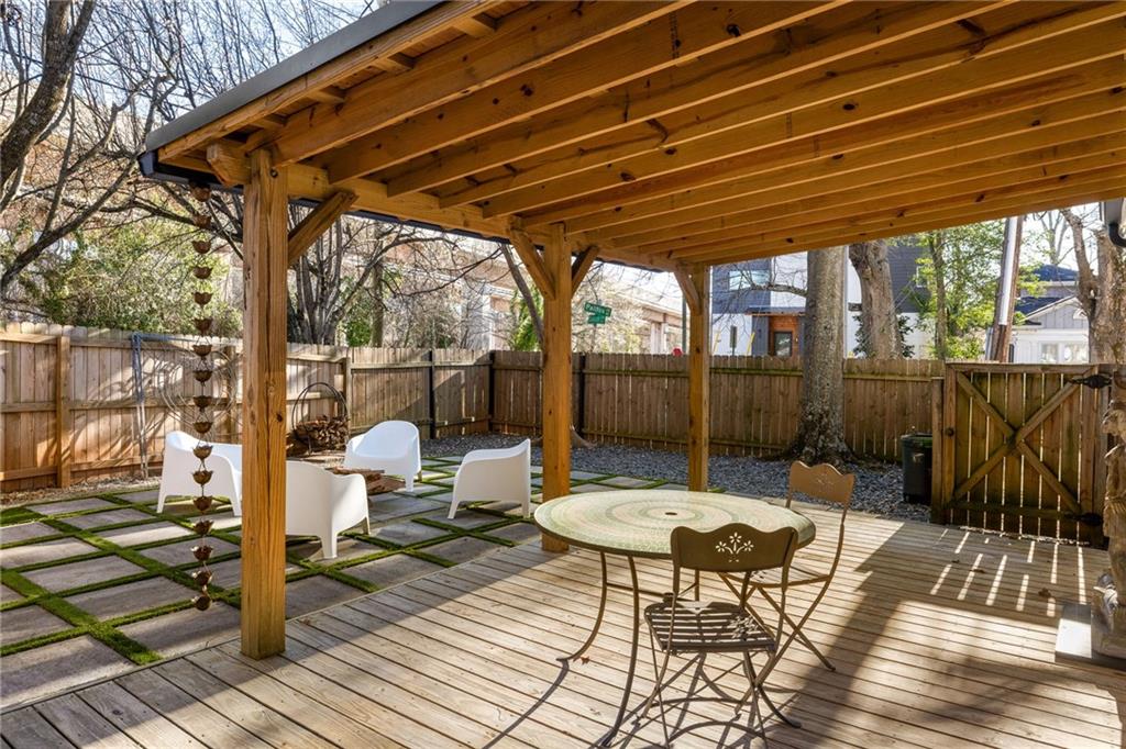Covered backyard patio with a timber pergola, wooden deck, outdoor dining set, and paved seating area.