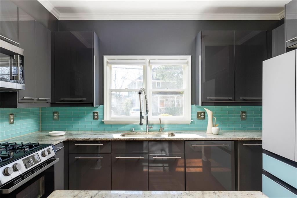 Kitchen with turquoise tile backsplash, dark cabinets, and sink beneath a double window.