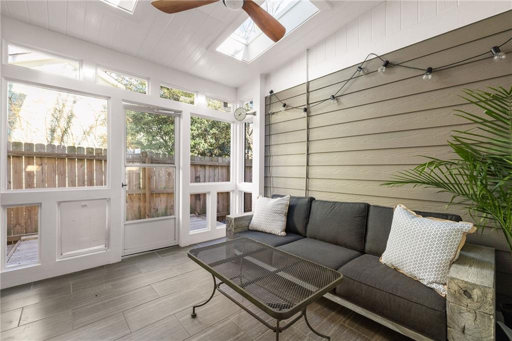Sunroom with a dark sofa, gray tile floor, wood-paneled wall, and large windows.