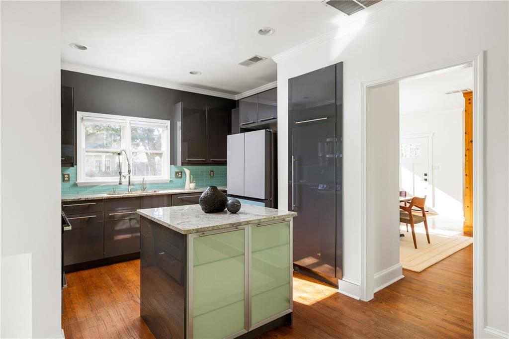 Kitchen with turquoise backsplash, dark cabinets, and pale green island overlooking a sunlit dining area.