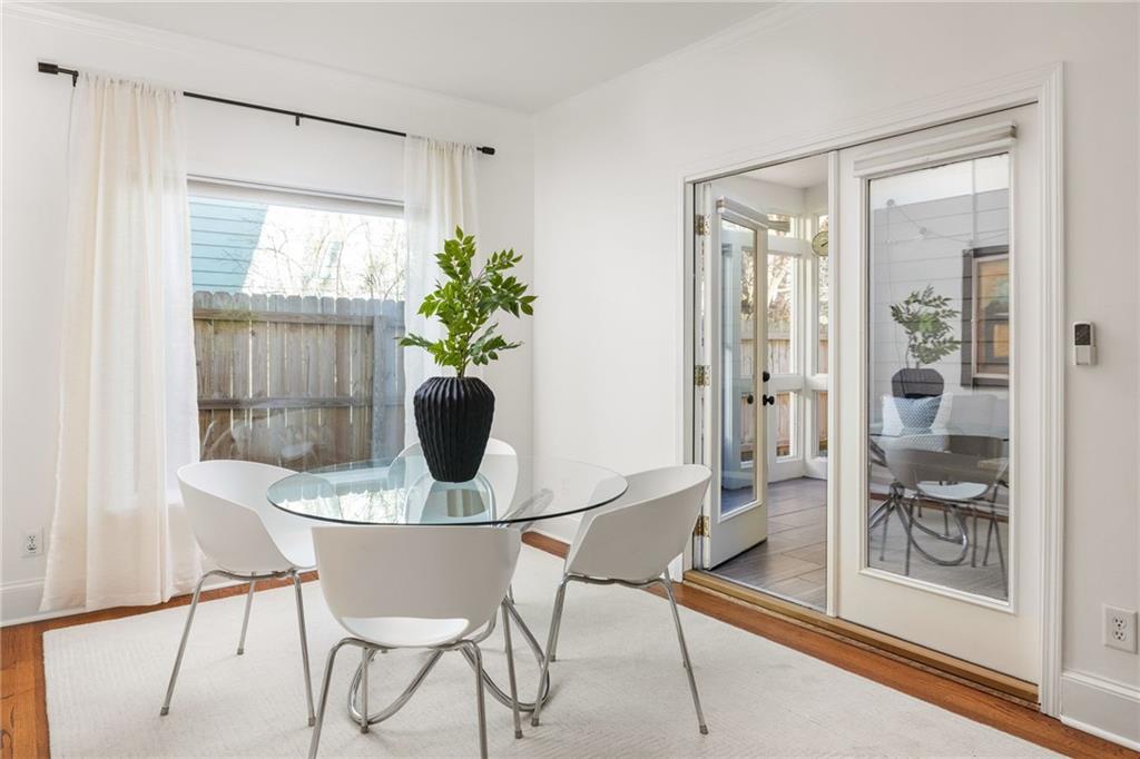 Dining room with a round glass table and white chairs beside glass doors to a sunroom.