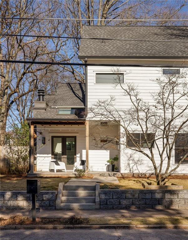 White two-story house with a covered porch, dark double doors, and stone steps from the sidewalk.