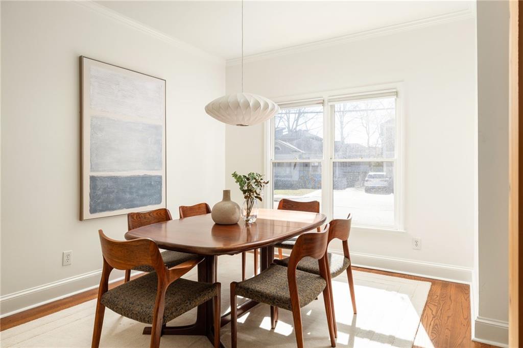 Dining room with a wooden table, upholstered chairs, and large sunlit windows.