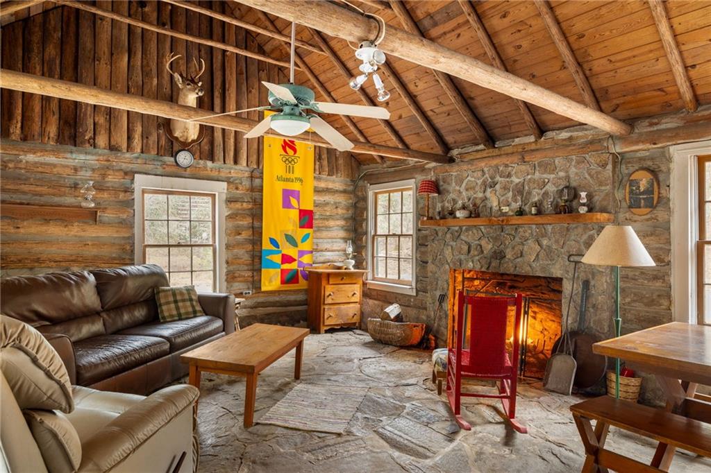 Rustic cabin living room with a stone fireplace, log walls, and a vaulted wood ceiling.