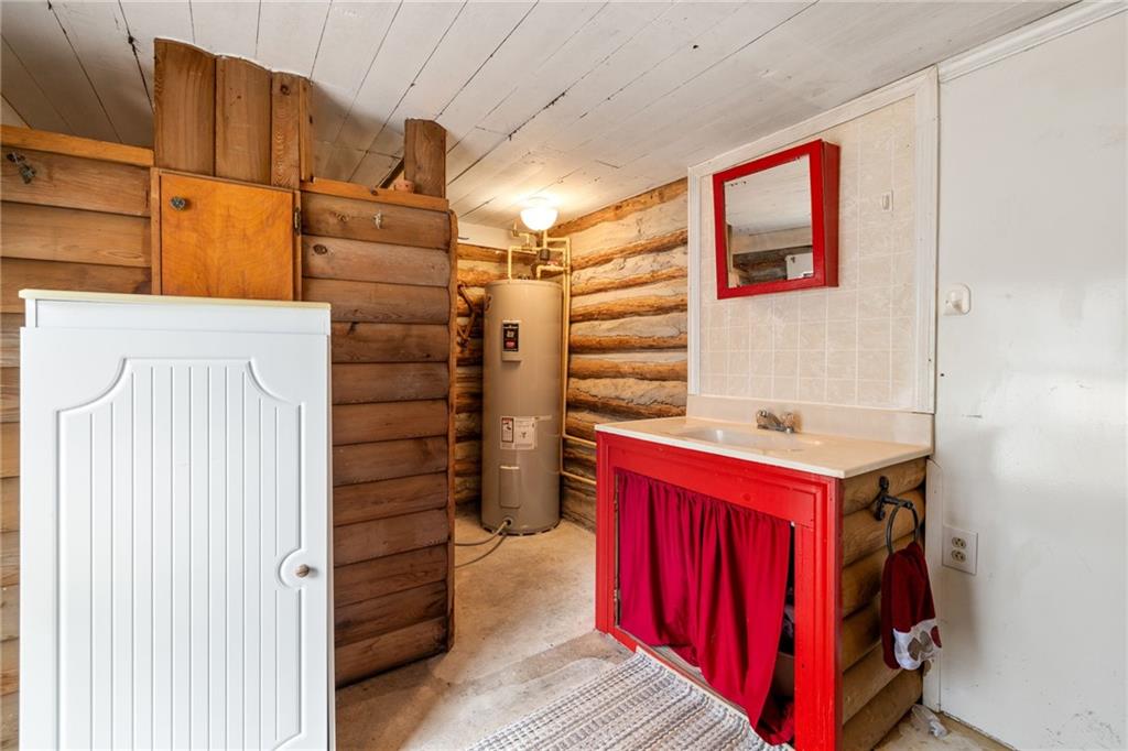 Log-cabin bathroom with a red vanity and curtain beside a water heater.