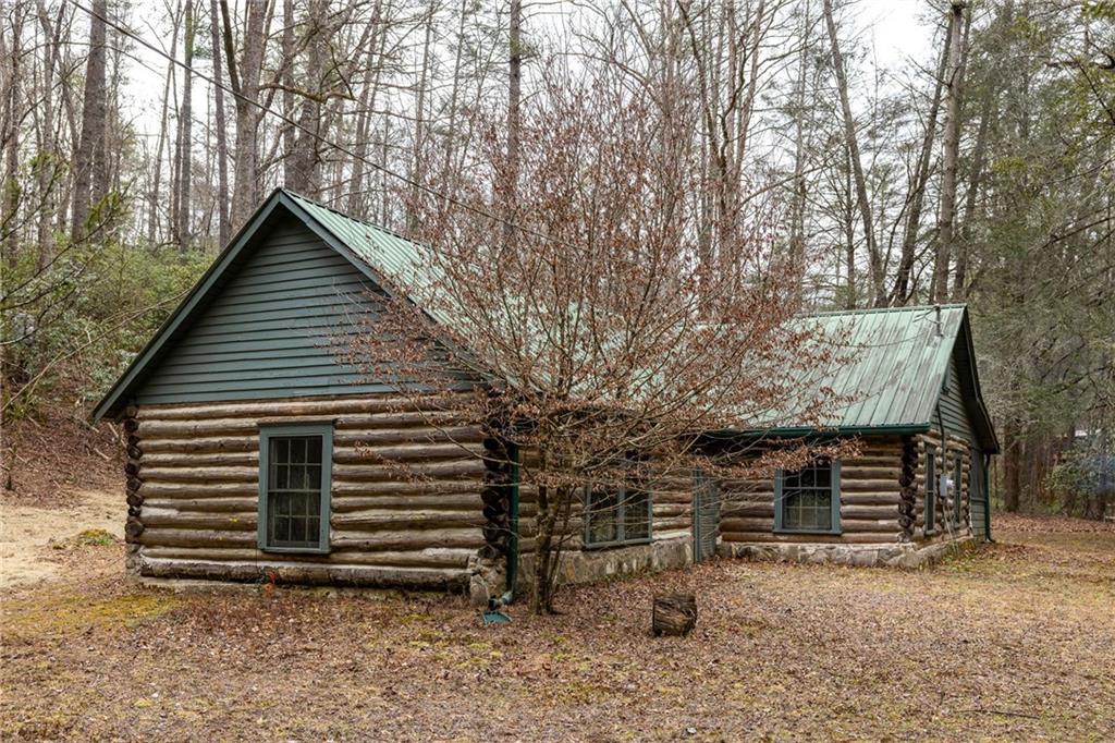 Log cabin with a green metal roof among leafless trees.