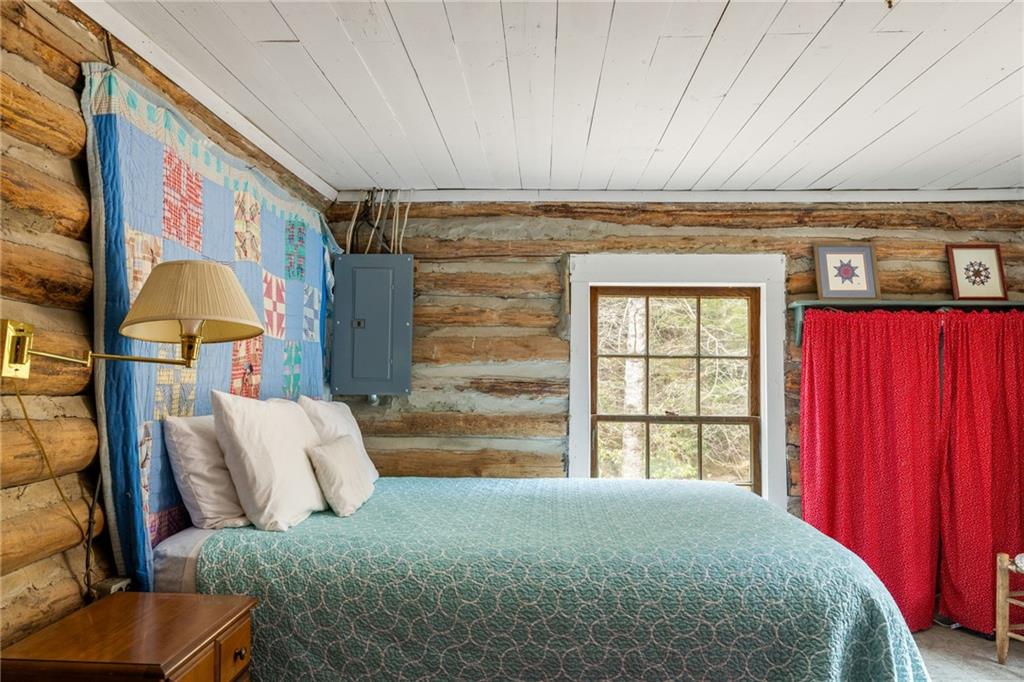Log-cabin bedroom with a teal quilt, patchwork wall quilt, and red curtains.