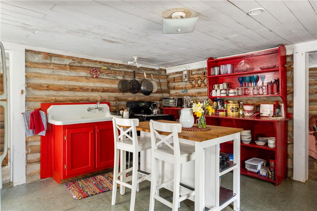 Rustic log-walled kitchen with red cabinets and a white island with wooden countertop.