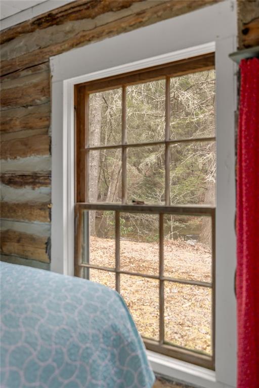 Divided-light window in a log-walled room overlooking trees and a small creek.