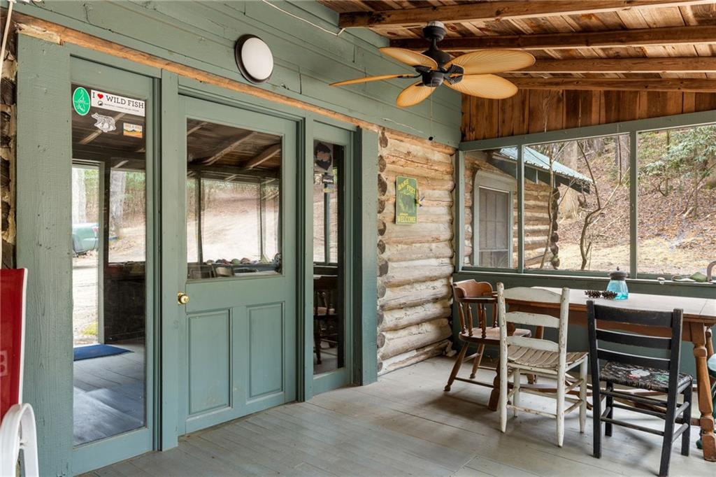 Rustic porch with green double doors, log walls, and a dining table beside large windows.