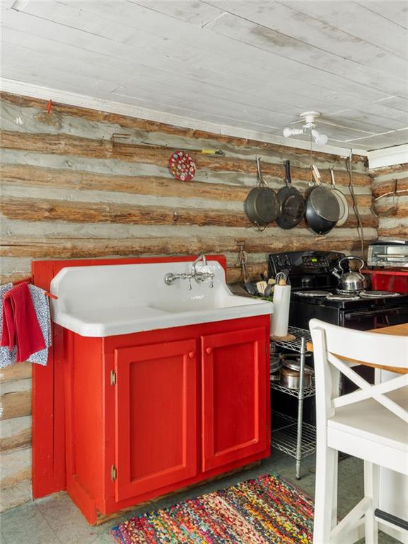 Cabin kitchen with a red sink cabinet, farmhouse sink, hanging pans, and black stove.