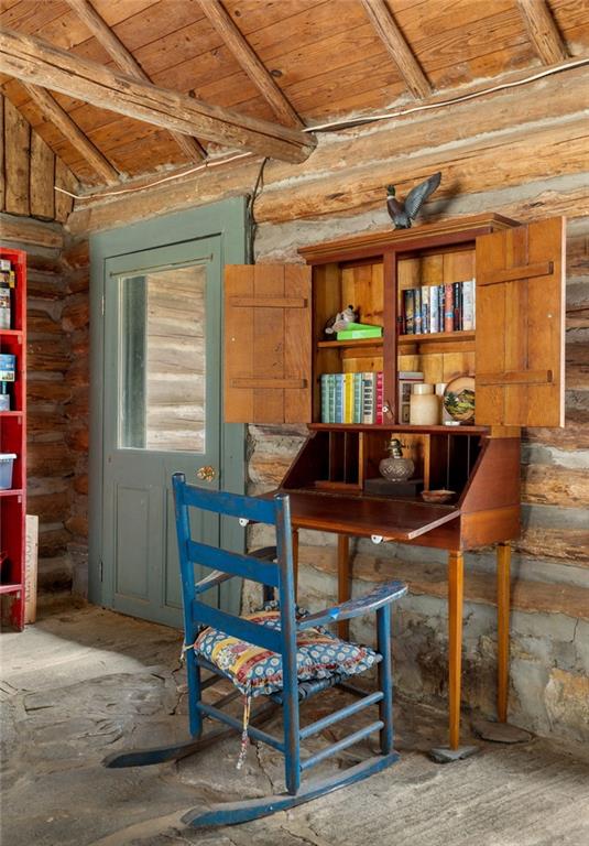 Rustic cabin office with a wooden writing desk and bookcase, blue chair, exposed logs, and stone floor.