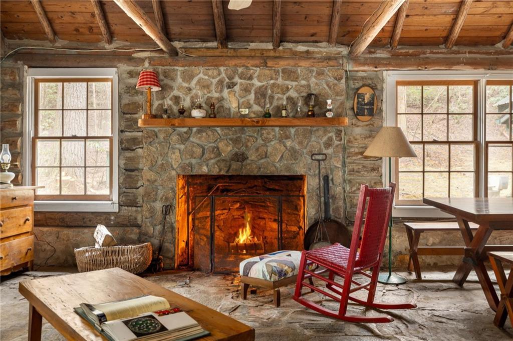Rustic living room with a lit stone fireplace, exposed beams, and a red rocking chair.