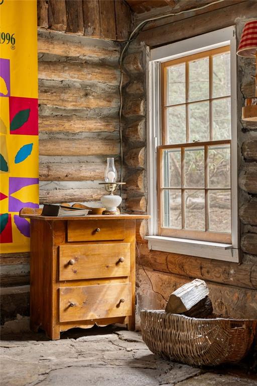 Log cabin interior with a wooden chest, divided-pane window, and basket of firewood.