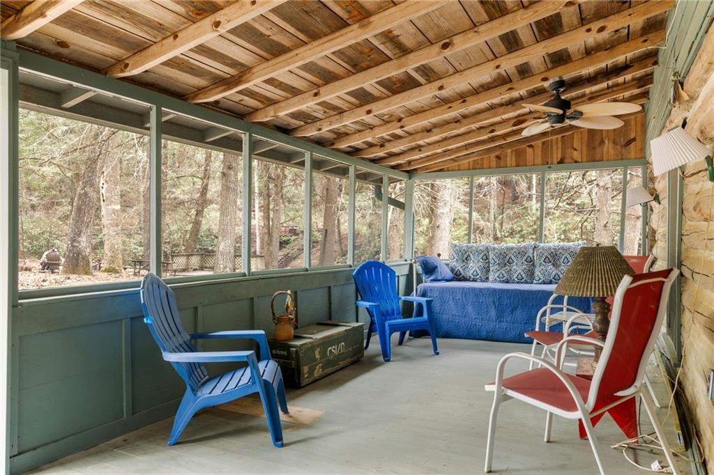 Screened porch with colorful seating, exposed wood ceiling, and wooded views.