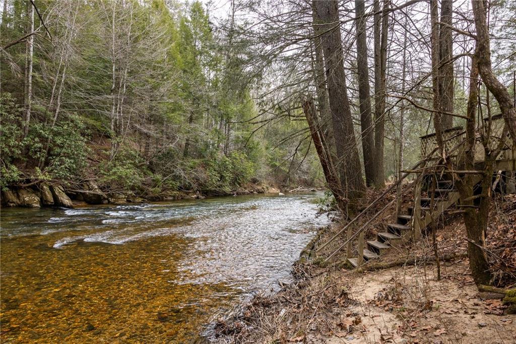 Rocky creek flowing beside a wooded bank with wooden steps leading down to the water.