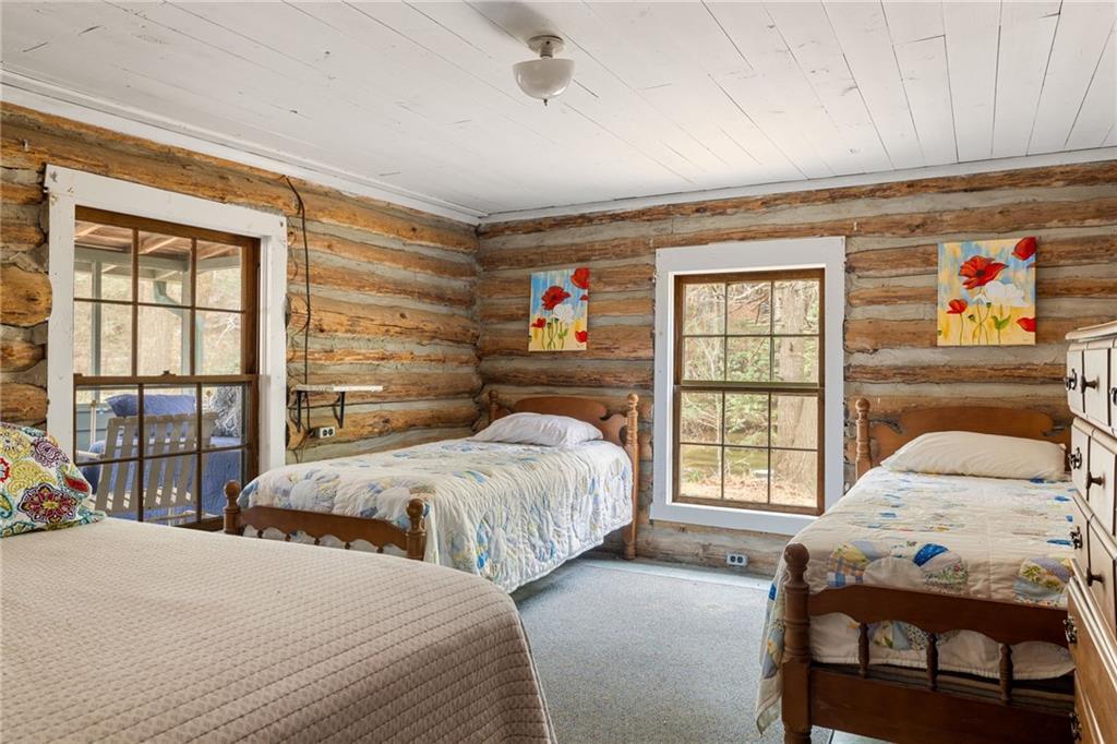 Rustic log-cabin bedroom with three beds, exposed log walls, and windows overlooking trees.