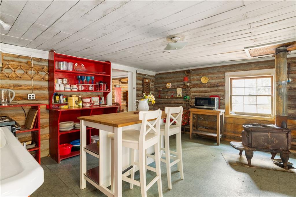 Rustic log cabin kitchen with a red open cupboard, island seating, and cast-iron wood stove.
