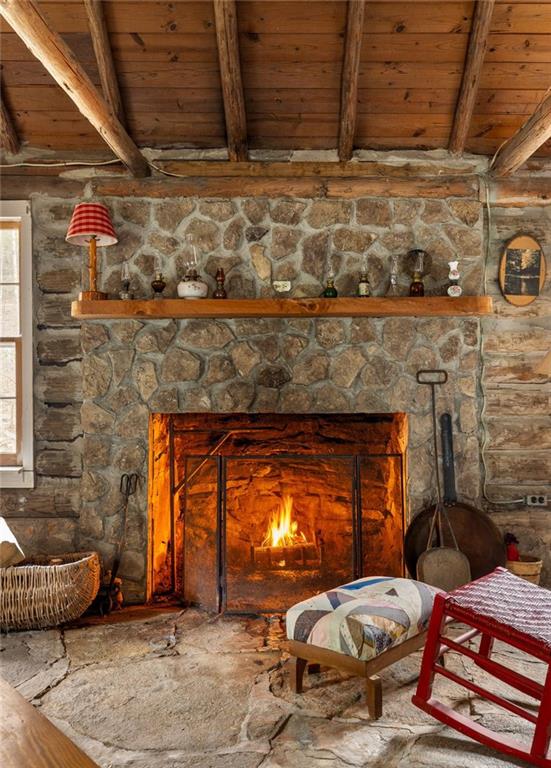 Rustic living room with a glowing stone fireplace, exposed timber ceiling, and log walls.