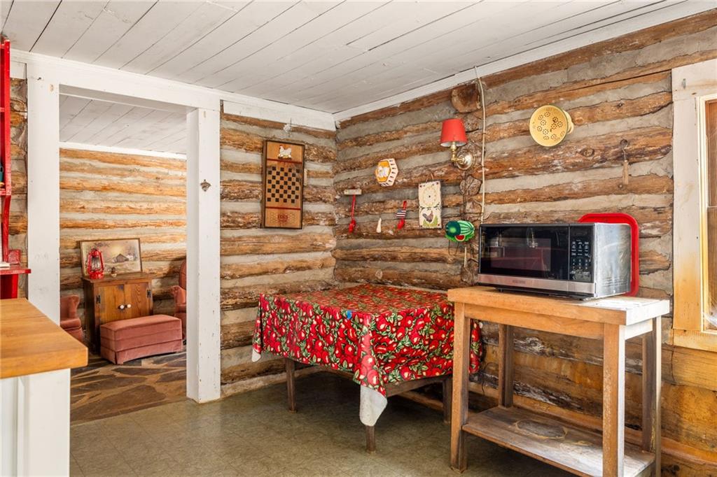 Rustic log cabin kitchen with exposed log walls, a red patterned tablecloth, and a microwave on a wooden table.