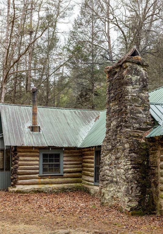 Rustic log cabin with a pale green metal roof and a large stone chimney among bare trees.