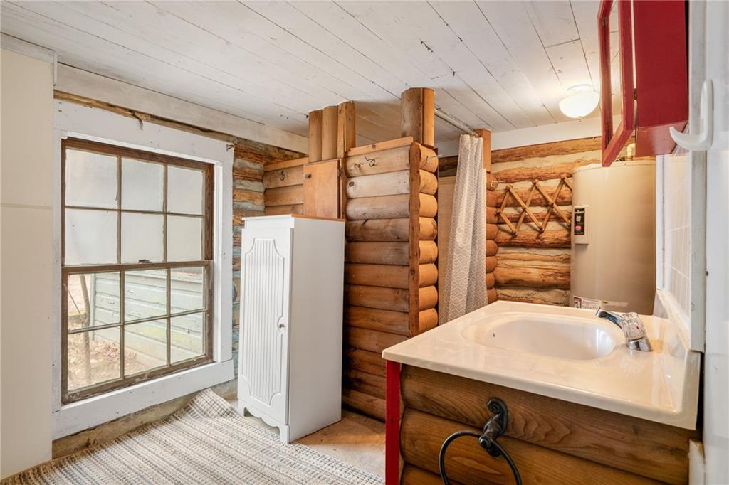 Rustic log-cabin bathroom with a white sink, wooden vanity, log walls, and a multi-pane window.