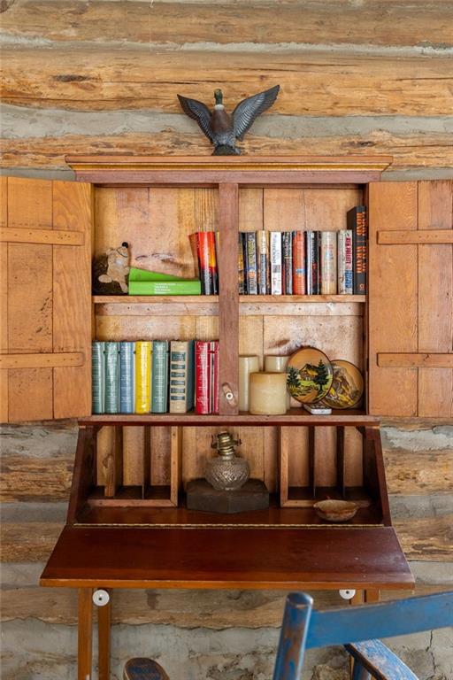 Wooden secretary bookcase filled with books and decor against a rustic log wall.