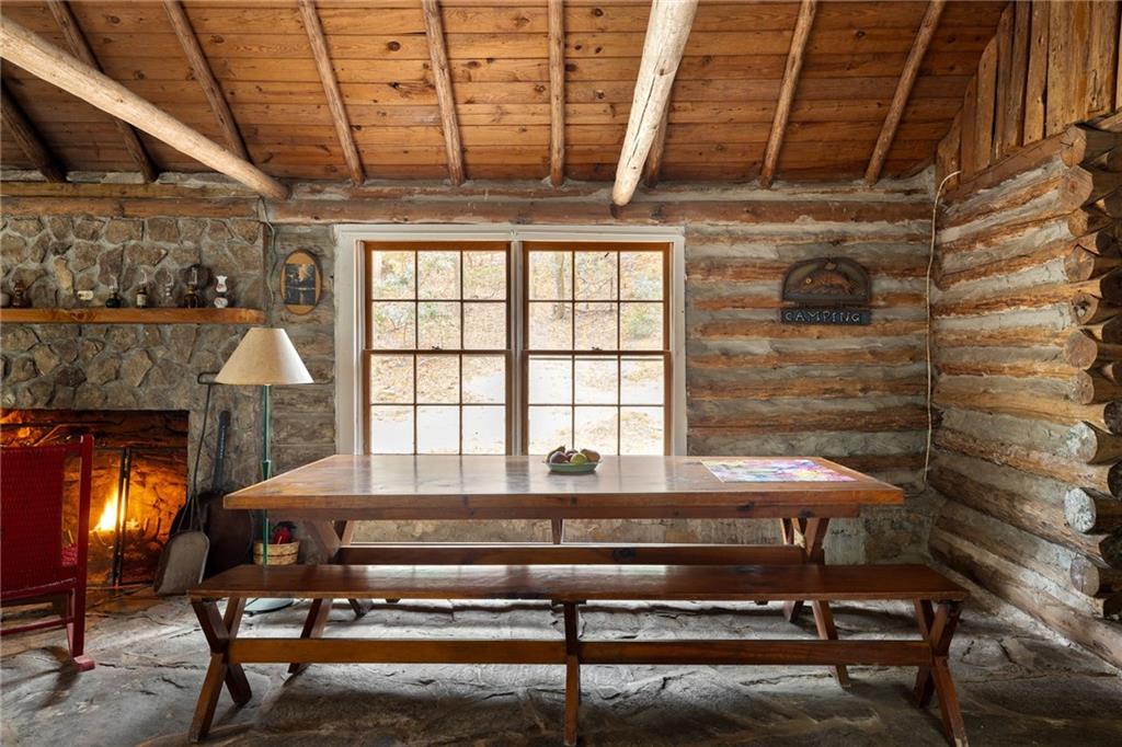 Rustic log cabin dining room with a wooden picnic table, large window, and lit stone fireplace.