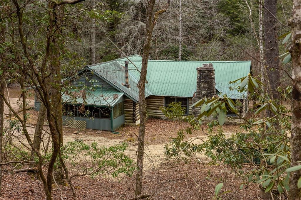 Woodland log cabin with a pale green metal roof, stone chimney, and enclosed porch.